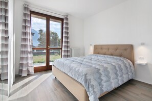 Une chambre à coucher avec un lit, une fenêtre avec des rideaux, un radiateur et une vue sur la verdure et les montagnes.
