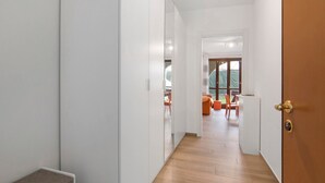 Ein Flur mit einer Bank, einer Tür und Blick in einen Raum mit Fenster und Stuhl.
