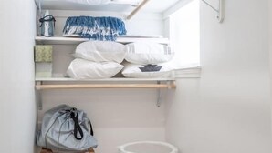A small, well-organized closet with shelves, a hanging rack, and storage bins. - Luxo Stays |Modern Studio| Near SFO, Westlake BART (Daly City)