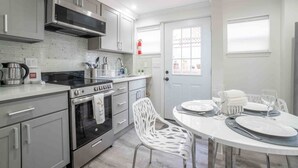 A modern kitchen with stainless steel appliances, a white tiled backsplash, and a dining area with a white table and chairs. - Luxo Stays |Modern Studio| Near SFO, Westlake BART (Daly City)