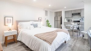 Une chambre d’hôtel moderne avec un lit bien fait, une petite table de chevet, une chaise et un coin cuisine.