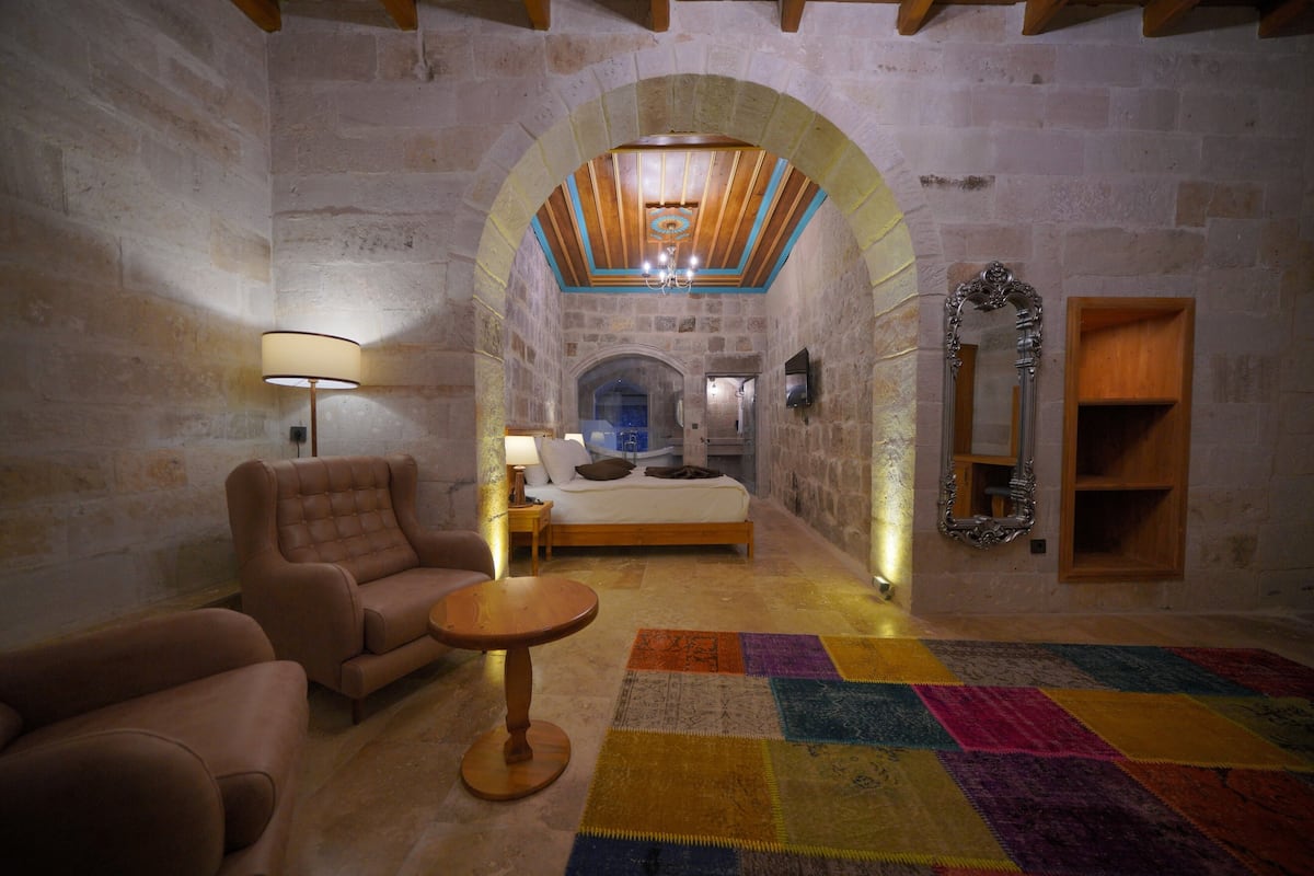 A cozy room with a bed, a sofa, a small table, and a colorful rug.