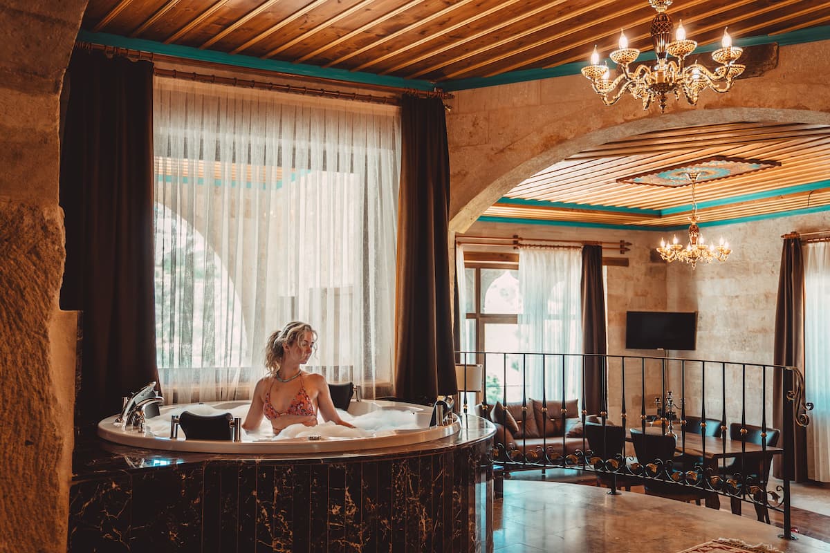 A room with a bathtub, a chandelier, and a television on the wall.