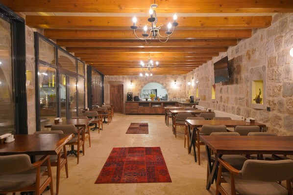 Un restaurant avec des tables et des chaises en bois, un tapis rouge, des murs en pierre et un lustre.
