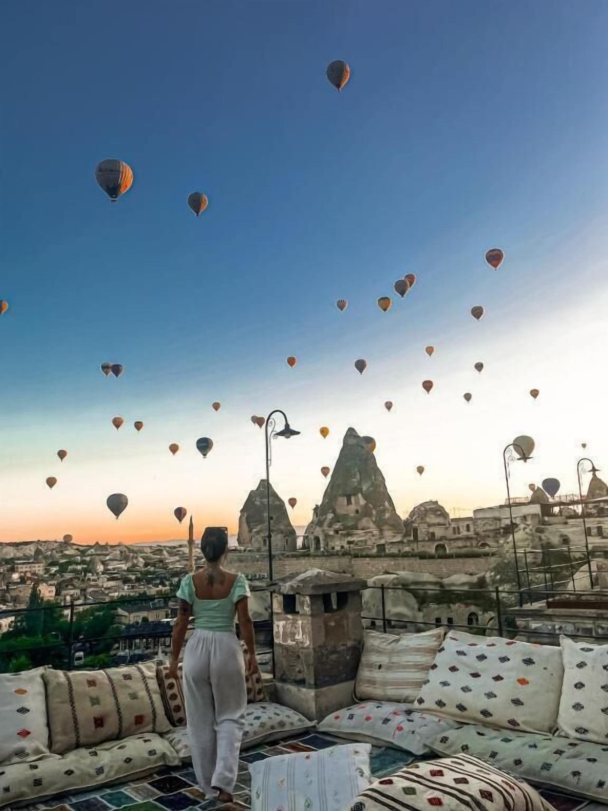 Iemand staat op een dakterrras en kijkt uit over een stadsgezicht met talloze luchtballonnen.
