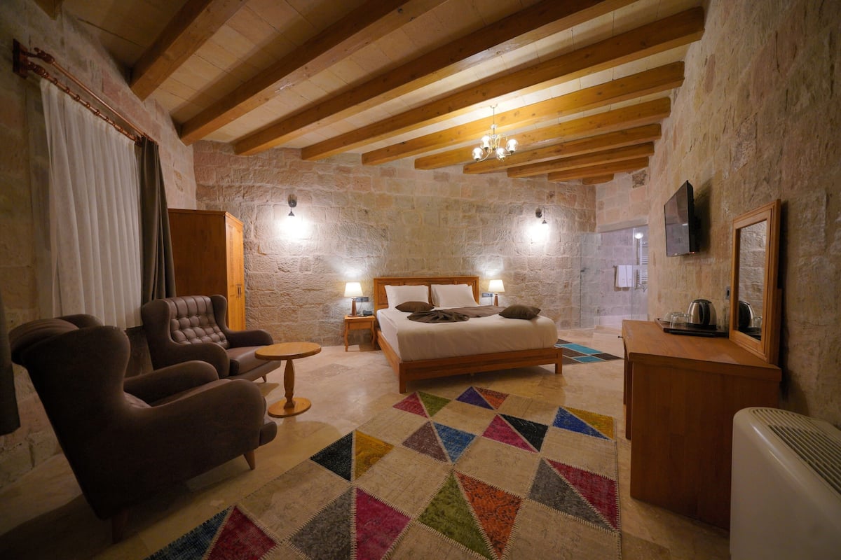 A bedroom with a bed, two bedside tables, a chair, a small table, and a TV on the wall.