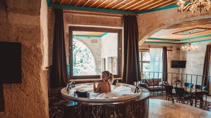 A luxurious bathroom with a marble bathtub, a large window, and a seating area with a chandelier. - Cappadocia Secret Hill Cave Suites (Nevsehir)