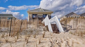 Ett hus vid stranden med en balkong, en trätrappa och en sandstrand i bakgrunden.
