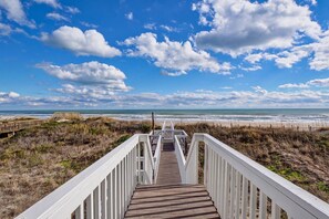 Une promenade en bois menant à une plage, avec un ciel dégagé et quelques nuages.