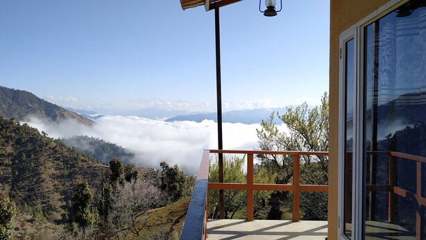 Un balcón con vistas a un paisaje montañoso, que incluye una zona boscosa y un valle cubierto de nubes.
