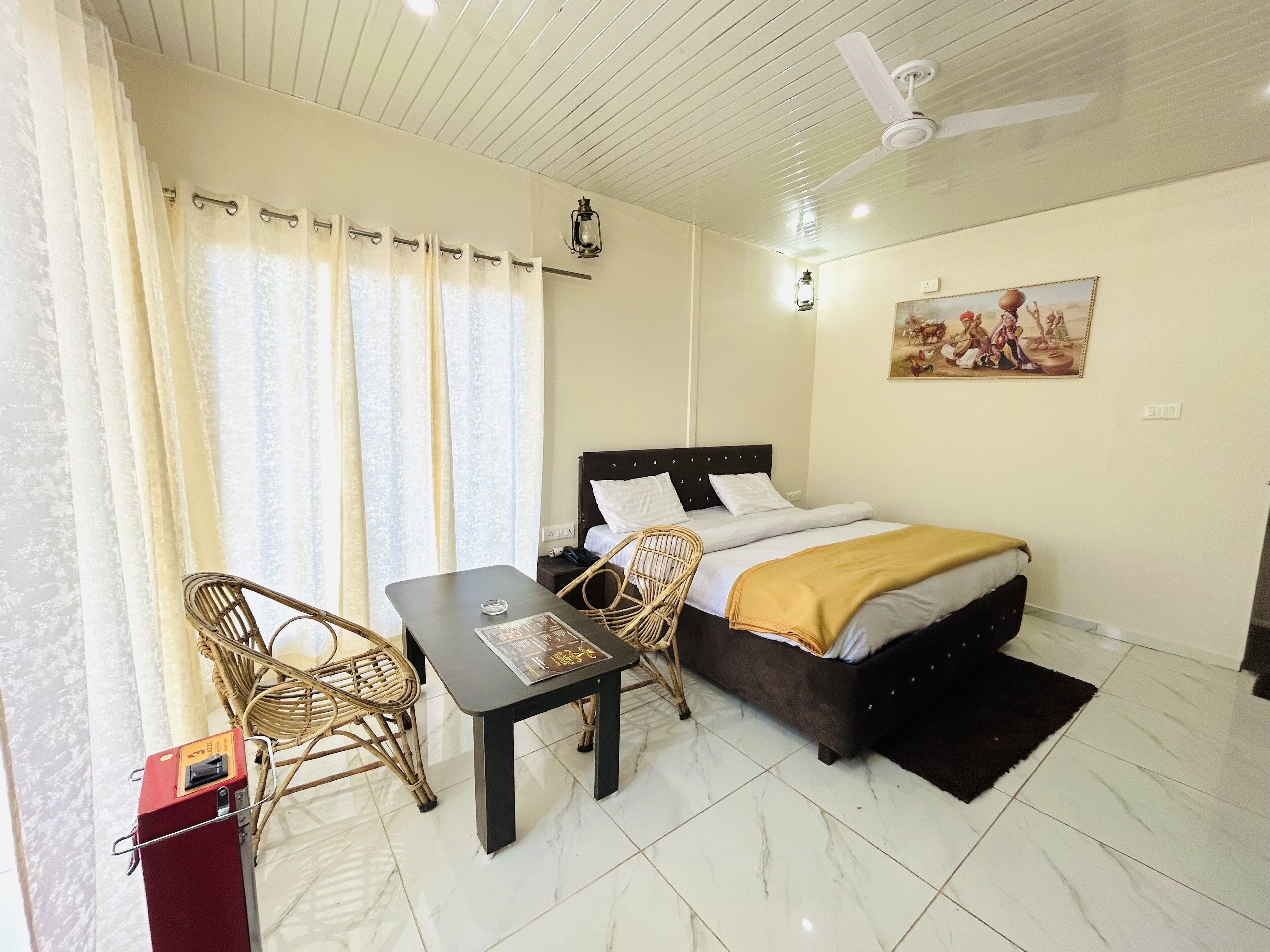 Una habitación de hotel con cama, una mesa, una silla, un ventilador de techo y un cuadro en la pared.