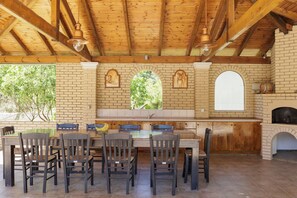 A brick patio with a wooden table and chairs, a brick fireplace, and a window with a view of trees. - Country Villa Verde (Corfu)