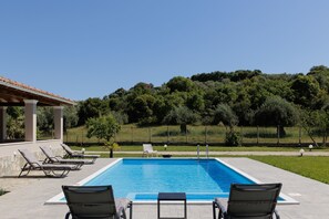 A rectangular swimming pool with clear blue water, surrounded by lounge chairs and a covered seating area. - Country Villa Verde (Corfu)