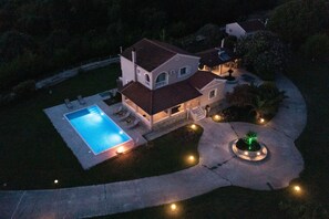 Een tweelaags huis met een zwembad, een overdekt terras en een aangelegde tuin.