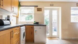 A compact kitchen with a washing machine, a dishwasher, and a window providing natural light. - Abbey House SW London for Big Groups (Colliers Wood)