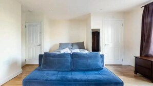 A bedroom with a bed, a blue sofa, and a wooden floor. - Abbey House SW London for Big Groups (Colliers Wood)