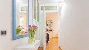 Un couloir avec une console blanche, un miroir et un vase orné de fleurs violettes.