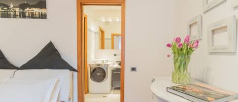A hotel room with a bed, a washing machine, and a vase with flowers.