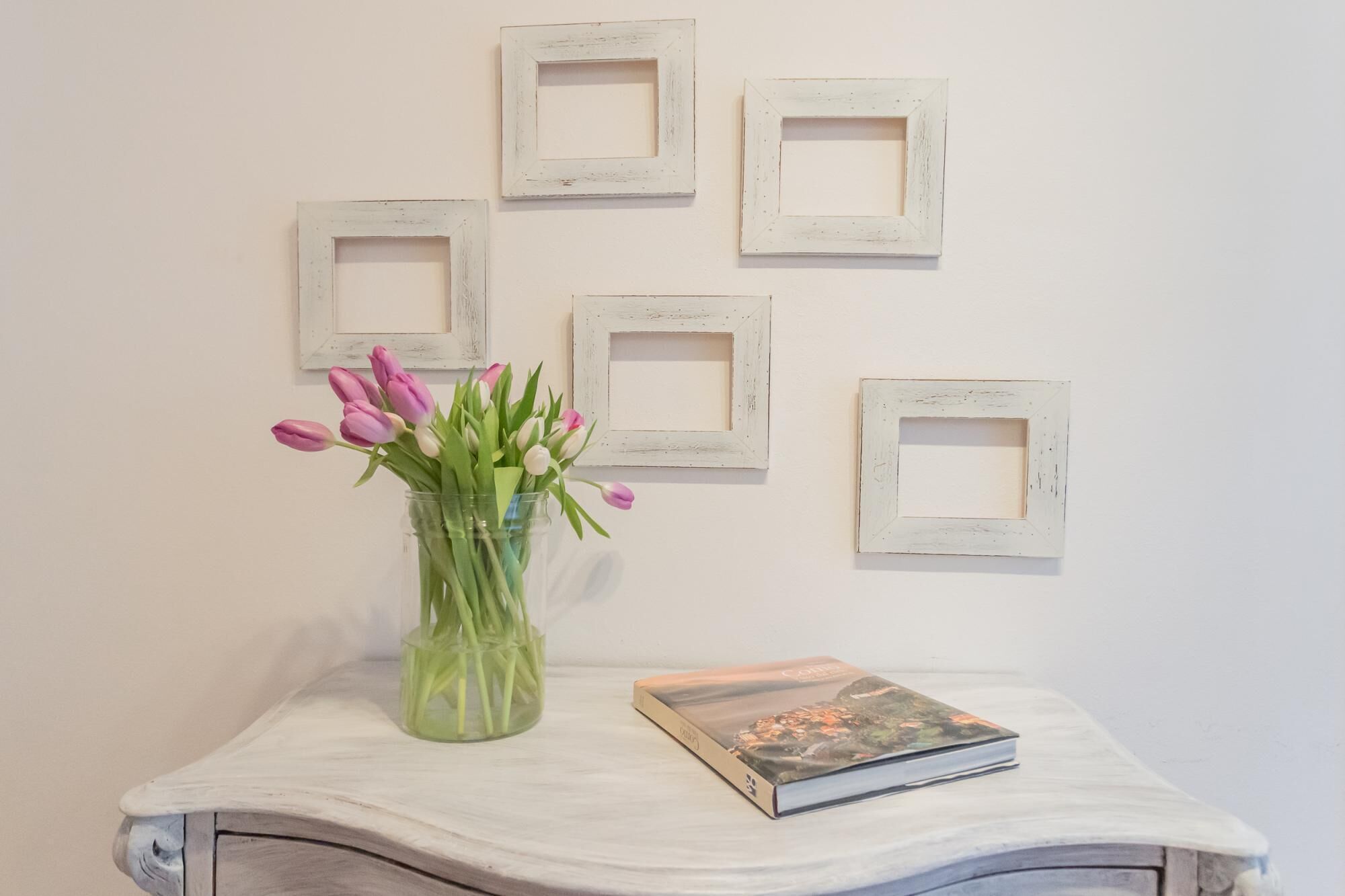 Ein weißer Tisch mit einer Vase voller pinkfarbener Tulpen und einem Buch.