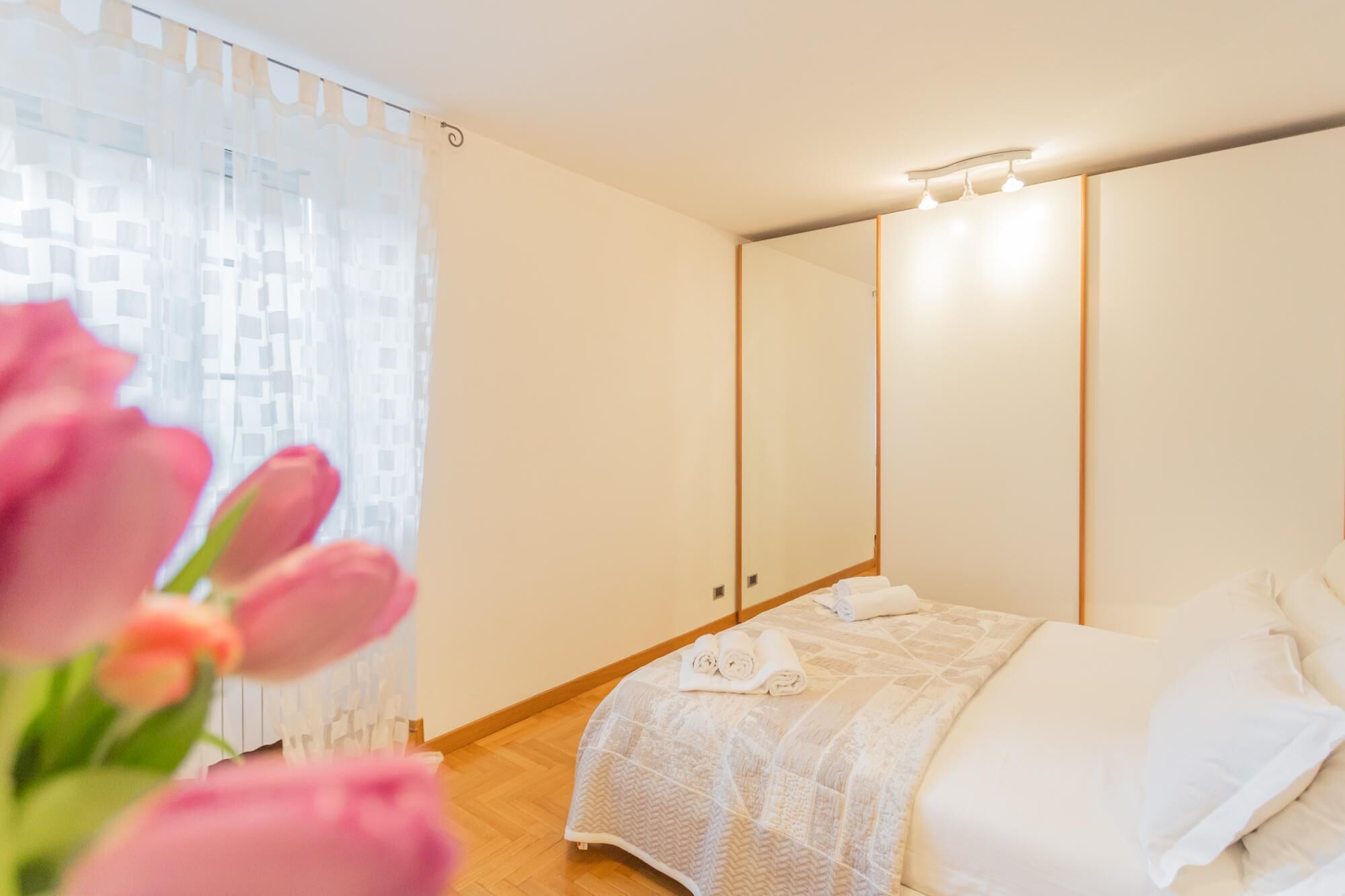 A bedroom with a bed, a large mirror, and a window with sheer curtains.