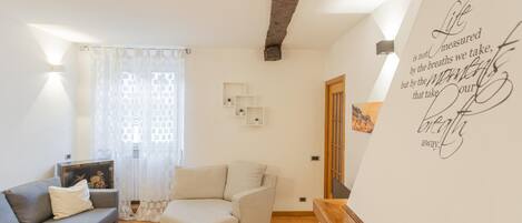 A living room with a grey sofa, a beige armchair, and a white coffee table. There is a wall with a quote and a door with a picture.