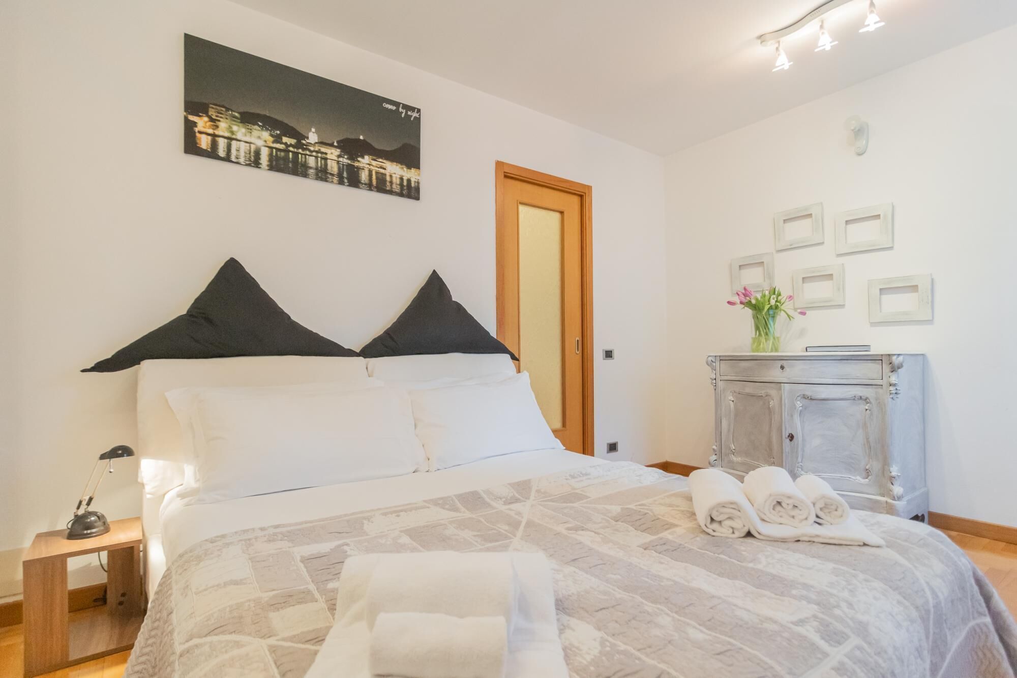 A bedroom with a bed, pillows, a nightstand, a lamp, a dresser, and a framed picture on the wall.