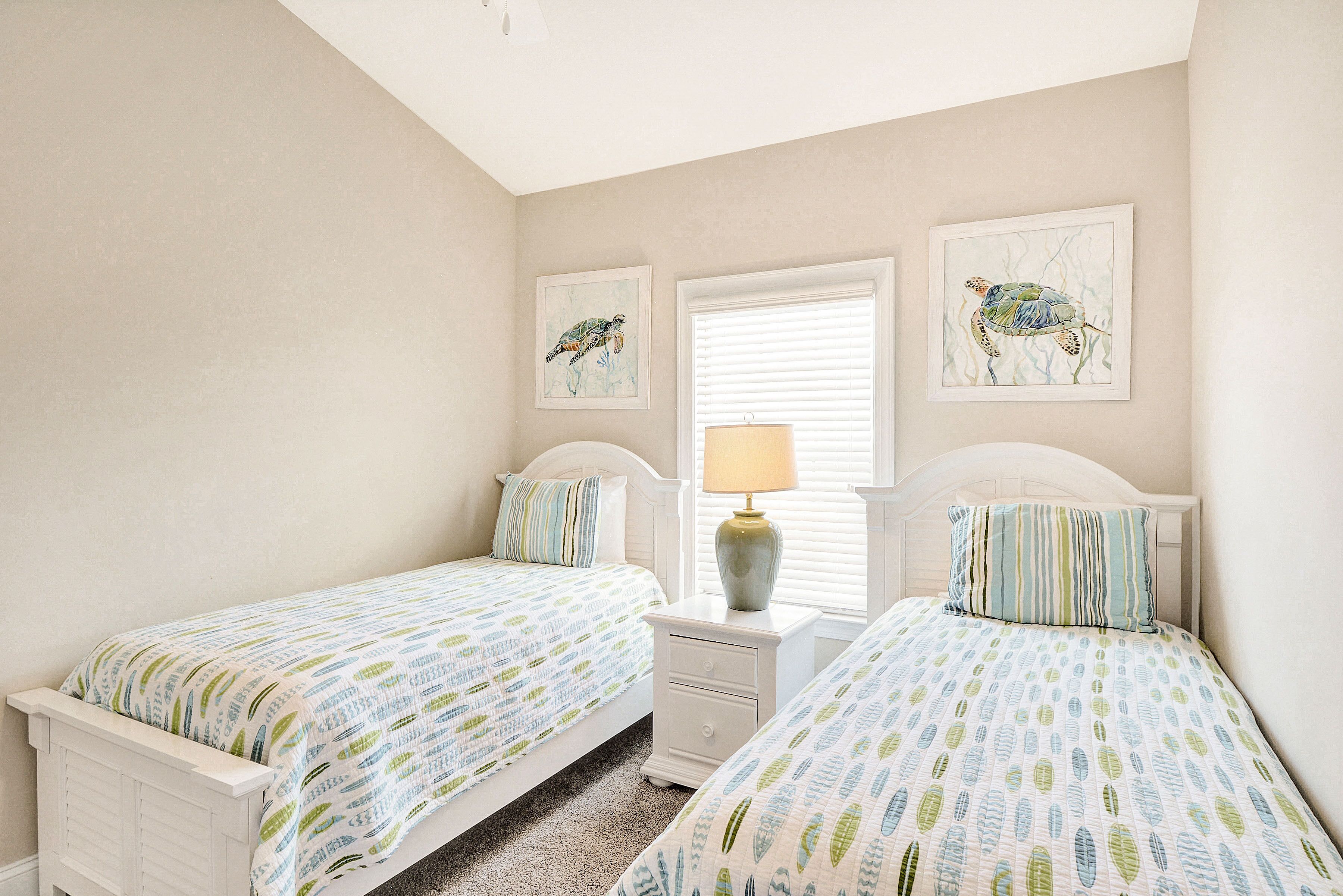 A bedroom with two beds, a nightstand with a lamp, and two framed pictures on the wall.