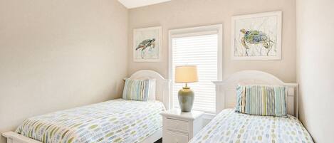 A bedroom with two beds, a nightstand with a lamp, and two framed pictures on the wall.