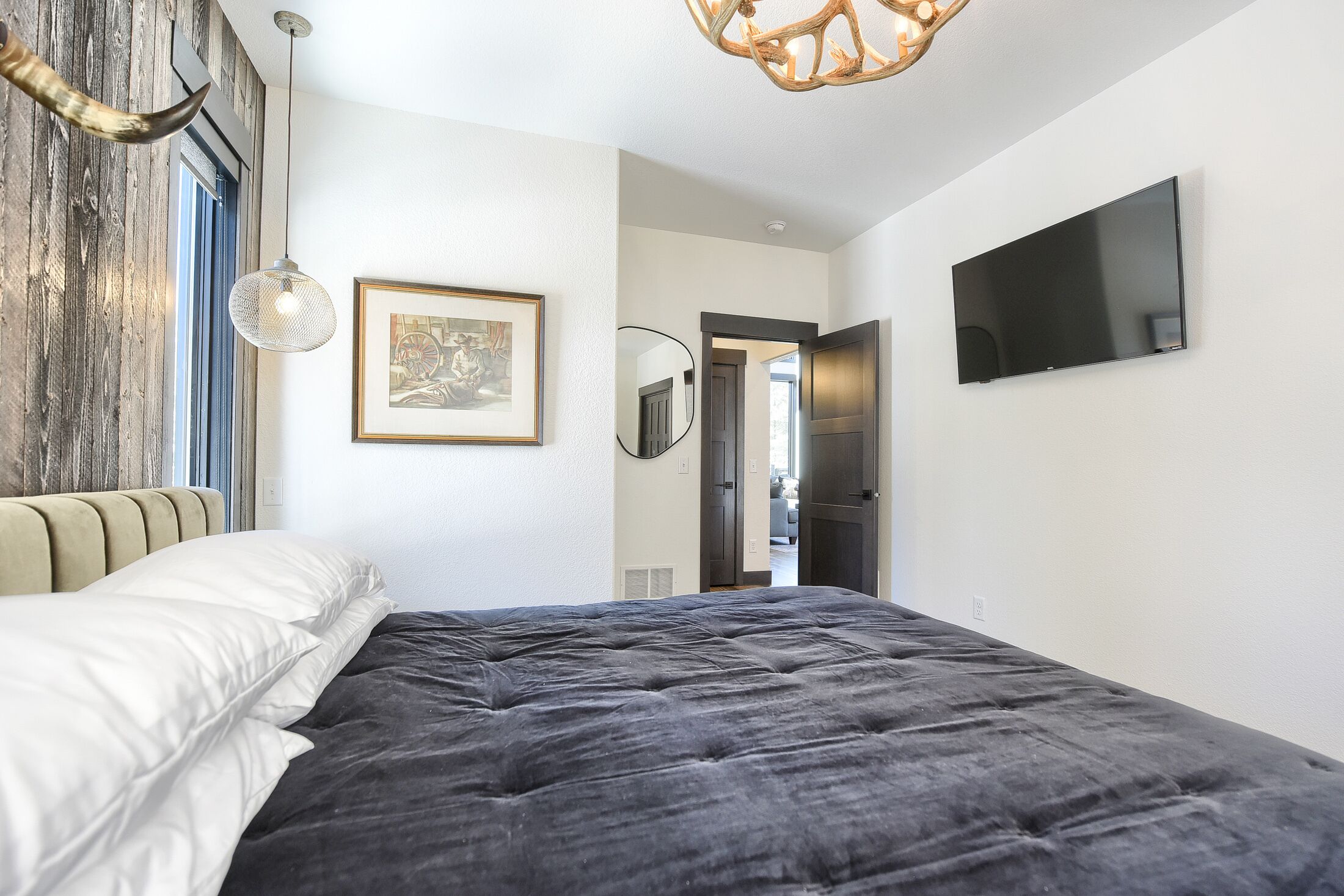 A bedroom with a large bed, a mounted TV, a framed picture on the wall, and a wooden accent wall.