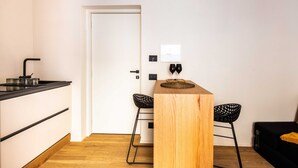 Eine kleine Küche mit Holzarbeitsplatte, zwei schwarzen Barhocker und einem Holztisch mit gewebter Tischmatte.