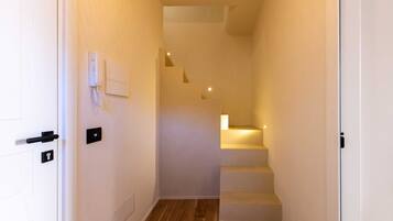 Ein schmaler Flur mit Holzboden, weißen Wänden und einer Treppe, die zu einer oberen Ebene führt.