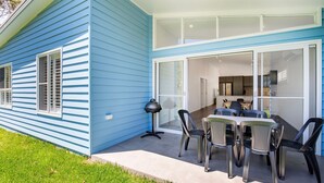 Een blauw huis met een patio, inclusief een tafel, stoelen, een barbecue en een glazen schuifdeur naar een keuken binnenshuis.