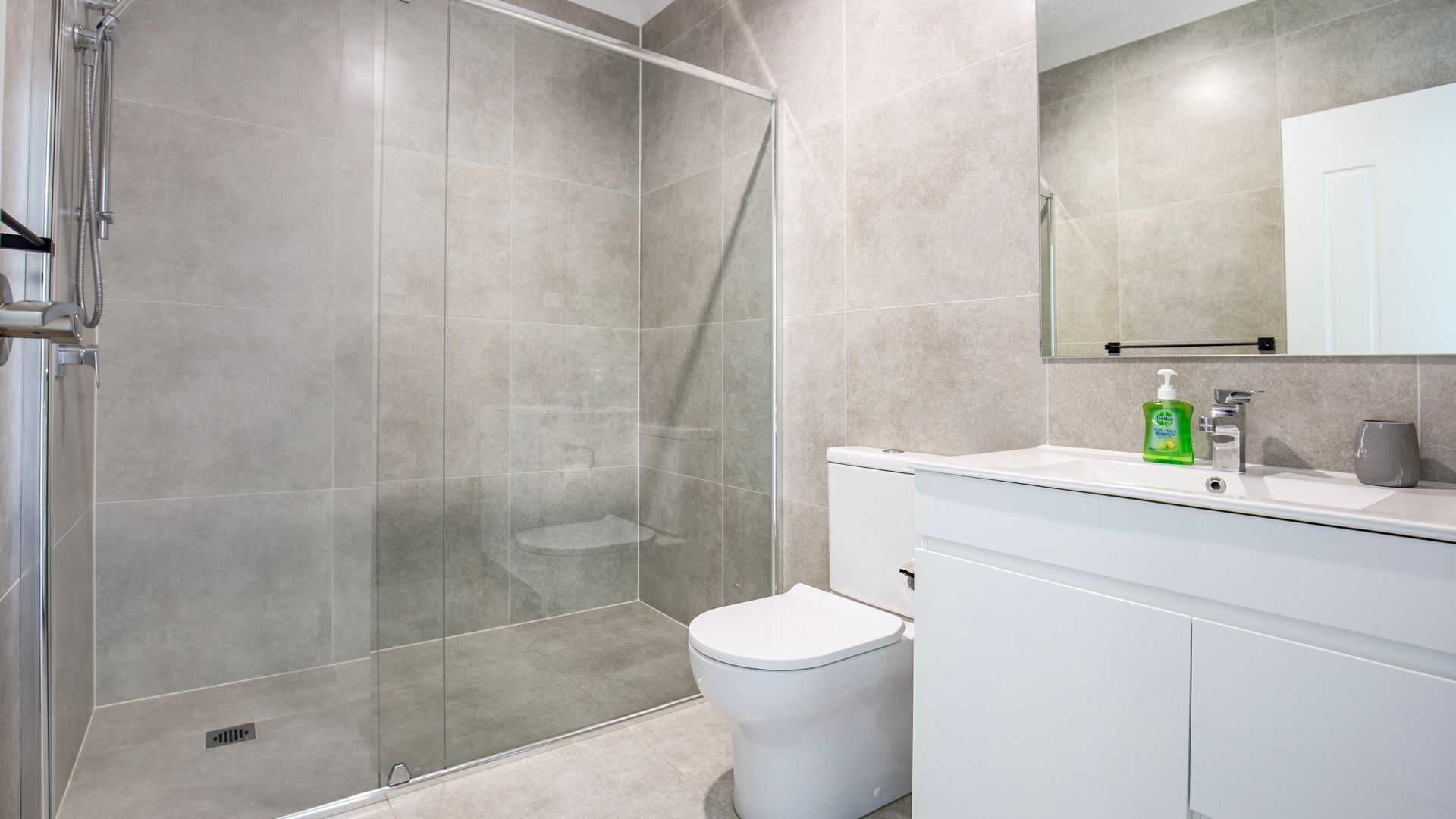 A modern bathroom with a glass shower enclosure, a white toilet, and a sink with a soap dispenser.