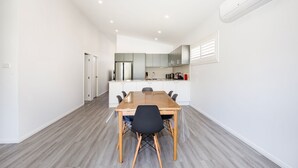 A modern kitchen with white cabinets, a central island, and a dining area with a wooden table and chairs. - Sanctuary Blue - Pet Friendly - 5 Mins to Hyams Beach (Sanctuary Point)