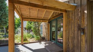 A wooden building with a covered porch, a green door, and a small outdoor area with plants.
