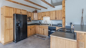 A kitchen with wooden cabinets, a black refrigerator, a dishwasher, a stove, and a sink.