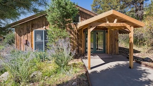 A wooden cabin with a covered porch and a glass door, surrounded by natural vegetation.