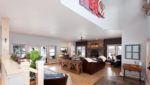 A spacious living area with a stone fireplace, wooden furniture, and large windows. - Rancho Sendero Correo -Historic Home on 300 Acres- Hot Tub/Pool Table/Trails (Hesperus)