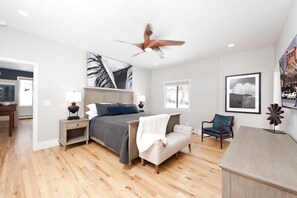 Cozy retreat with a large bed, nightstands, and a ceiling fan, set amidst framed artwork and a comfortable seating area.