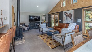 A cozy living room with a fireplace, leather furniture, and a large window with a horse painting. - Rancho Sendero Correo - Historic Home & Cabin on 300 Acres - Hot Tub (Hesperus)