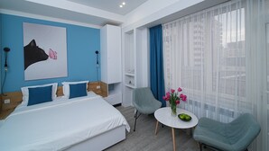 A modern hotel room with a large bed, a desk with a vase of flowers, and a view of the city through sheer curtains. - Cozy & Modern Studio with Balcony in the center of Yerevan by Sweet Home (Yerevan)