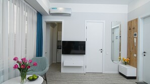 A modern living room with a flat-screen TV, a white cabinet, a blue armchair, and a small table with a vase of flowers. - Cozy & Modern Studio with Balcony in the center of Yerevan by Sweet Home (Yerevan)