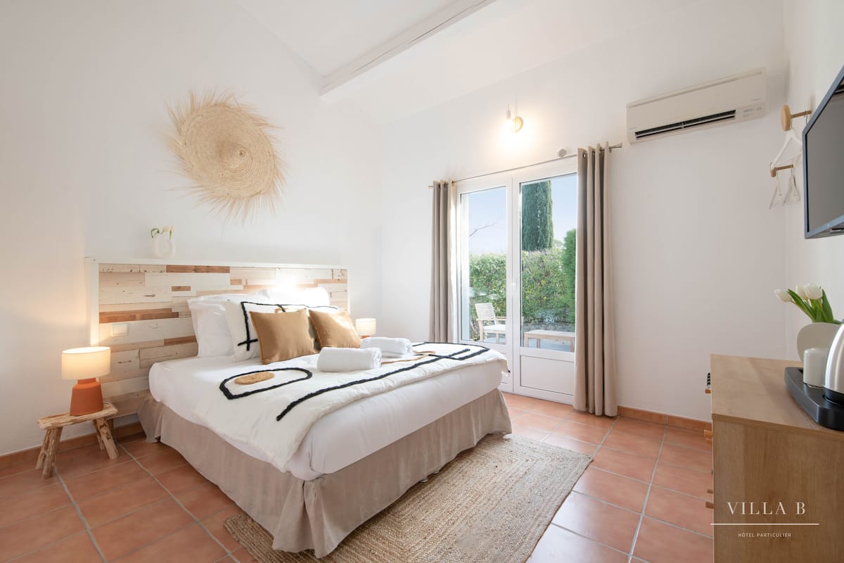 Una moderna camera d'hotel con un letto grande, un comodino con una lampada, una TV a parete e vista all'esterno tramite una porta scorrevole in vetro.