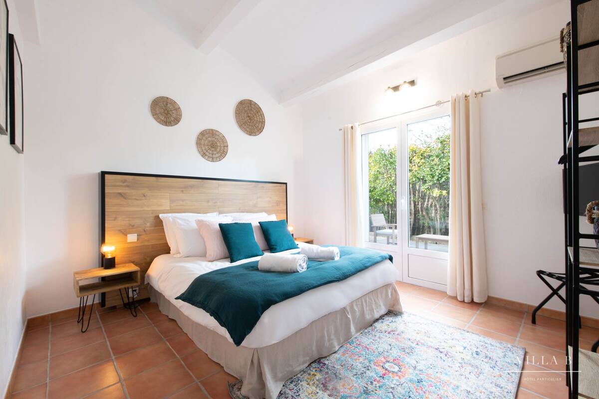 Una camera da letto con un letto grande, un comodino, una finestra con tende e vista su del verde all'esterno.
