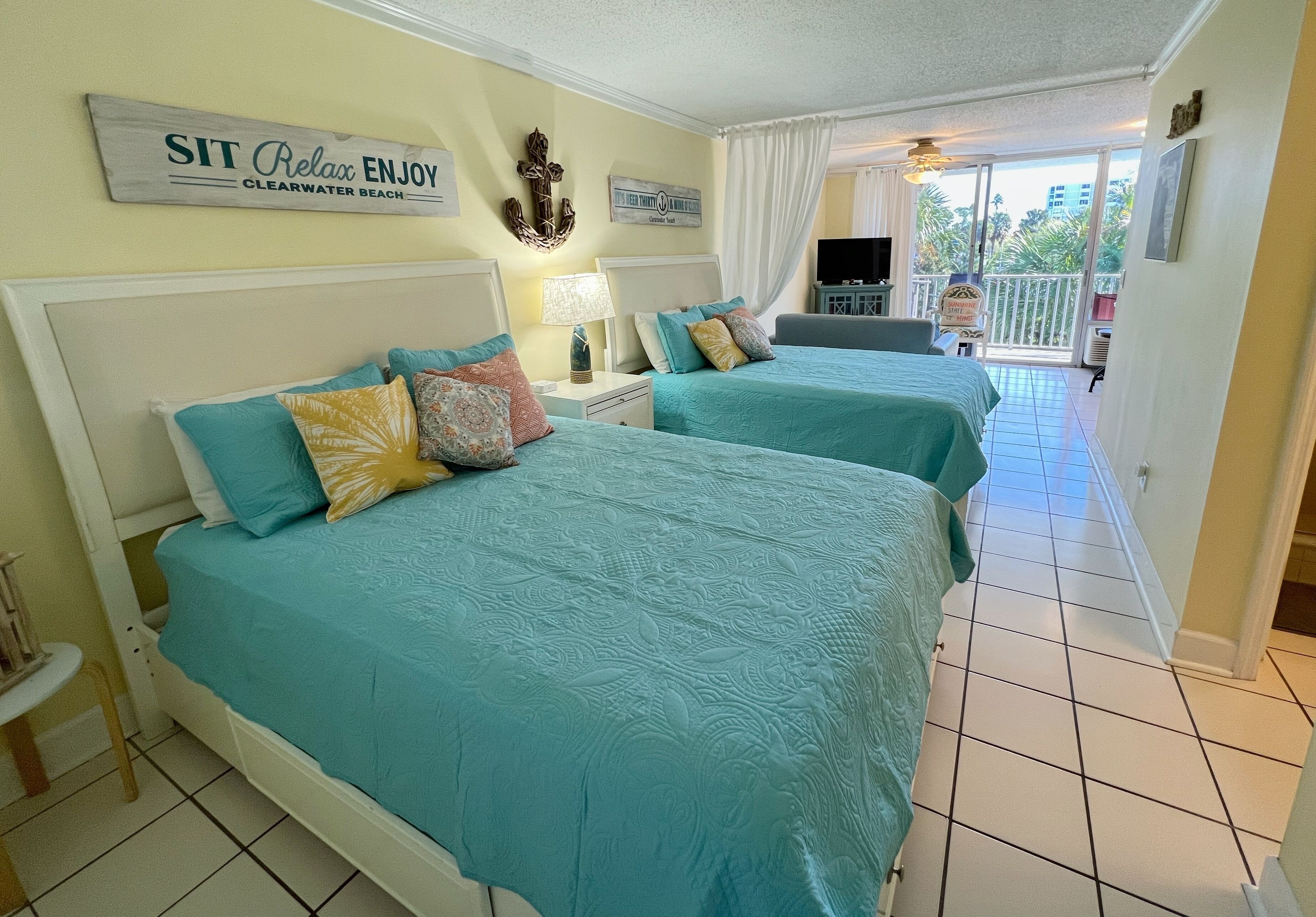 Ein Hotelzimmer mit zwei Betten und einem Balkon, mit einem Schild, auf dem steht: SIT Relax ENJOY CLEARWATER BEACH.
