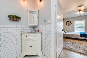 A bathroom with white subway tiles, a white vanity, a mirror, and a ceiling fan.