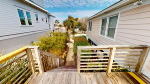A wooden staircase leading to a residential area with houses, a pool, and a clear sky. - 3 bedroom, 1 bath elevated home with private pool, walking distance to beach! (Isle of Palms)
