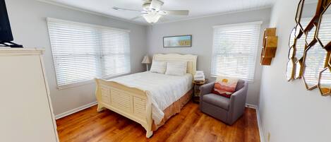 Un dormitorio con cama, una silla, una mesita de noche, una lámpara y un ventilador de techo.