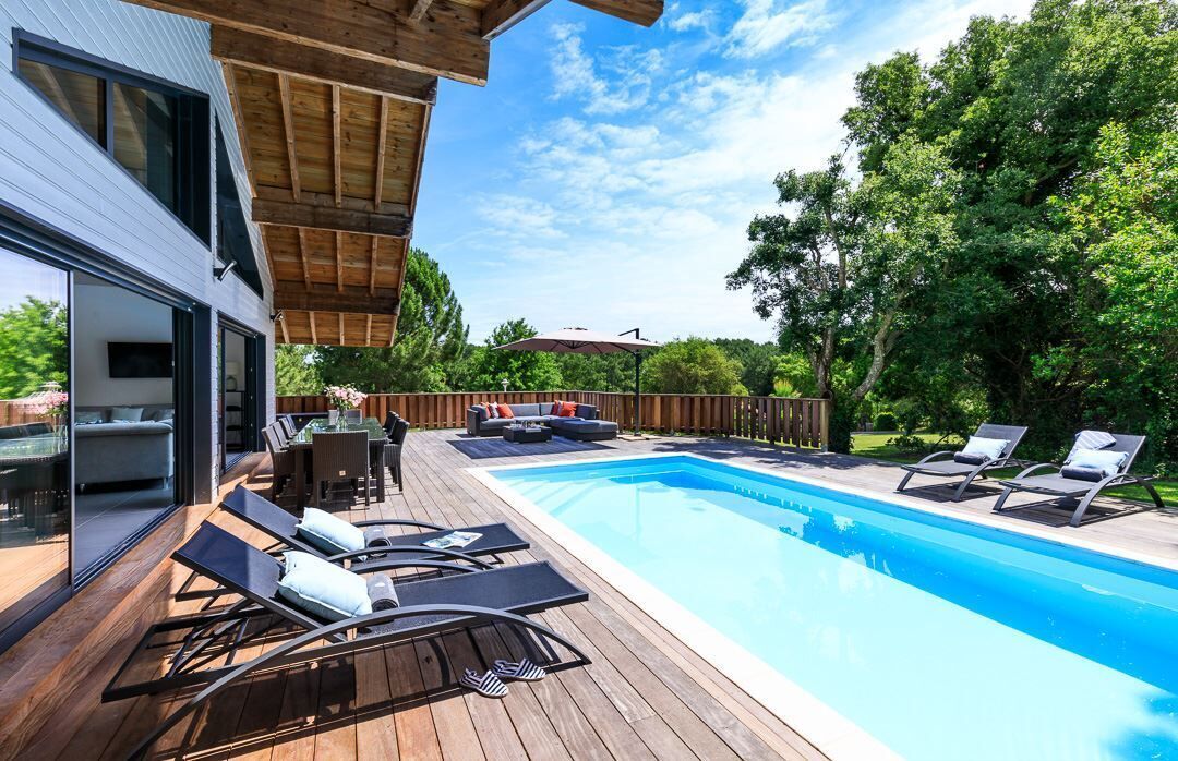 Een modern zwembad met ligbedden, een eettafel en een houten terras.