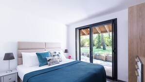 Un dormitorio moderno con una cama grande, una mesita de noche, una lámpara y un ventanal corredero que da a un espacio exterior.